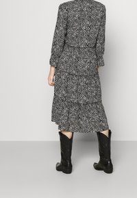 Abito a maniche lunghe con motivo bianco e nero, design a strati e orlo svasato, abbinato a stivali da cowboy neri alti fino al ginocchio.