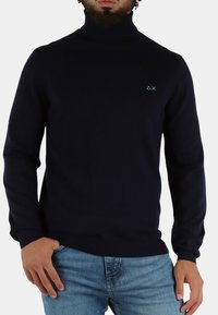 Maglione a collo alto blu navy in tessuto a coste con maniche lunghe, caratterizzato da un piccolo logo azzurro sul lato sinistro del petto e un design aderente.
