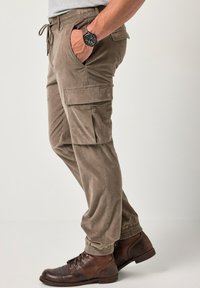 Bruine cargobroek met elastische manchetten en zijzakken, gemaakt van een zachte, getextureerde stof. Gemonteerd met bruine veterschoenen.