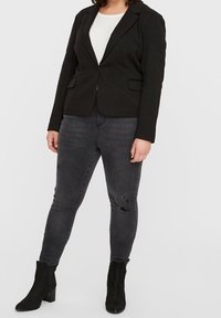 Blazer nero con revers sopra una maglia bianca, abbinato a jeans skinny grigio scuro strappati e stivaletti neri. Design aderente con tasche.