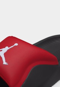 Czarna i czerwona sandał z paskiem typu slide z białym logo Jumpman na szerokim czerwonym pasku na górze.