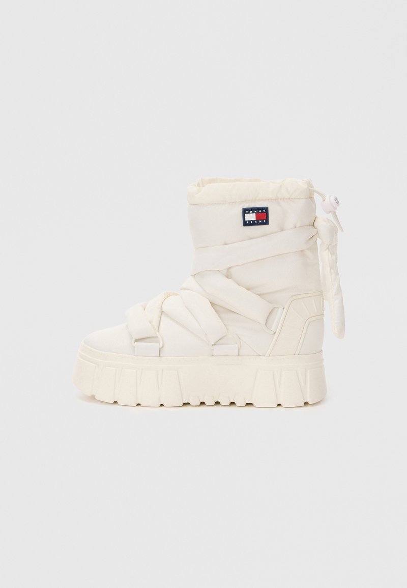 Botte blanche rembourrée avec une semelle épaisse, dotée de sangles en tissu et d'un patch logo sur le côté. Le design est à bout rond avec une texture douce.