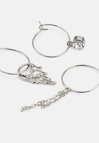 Brincos de argola em prata com um detalhe de cristal e um design em forma de mão, apresentando um pormenor de corrente, com um acabamento metálico moderno.