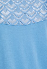 Indumento azzurro chiaro con un top in pizzo testurizzato a motivo scallop e una parte inferiore liscia dello stesso colore.