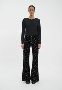 Haut noir à manches longues associé à un pantalon en velours évasé avec des motifs d'étoiles multicolores et des boutons à la taille. Chaussures noires.