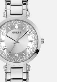 Hõbedane metallkell ümmarguse näoga, vääriskivide aktsentidega ja poleeritud viimistlusega. Omab minimalistlikku kelladiallit, kristallmärgiseid ja lingitud rihma.