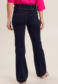 Jeans flared di un blu scuro con una vita alta, dotati di tasche anteriori e posteriori, e cuciture arancioni a contrasto lungo le cuciture.