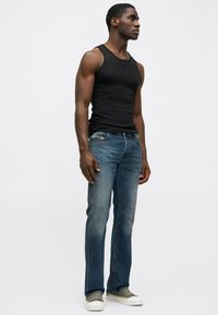 Camisola preta sem mangas, jeans azuis de perna reta de tamanho médio e ténis cinzentos com solas brancas. Detalhes mínimos nos jeans.