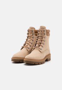 Botas de ante marrón claro hasta el tobillo con ojales reforzados, cuello acolchado y suelas de goma marrón con un patrón de tacos para mejor tracción.