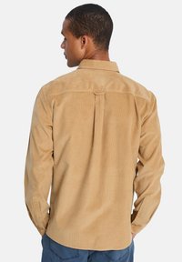 Ανοιχτό καφέ πουκάμισο από κορντόρι με πτυχώσεις στην πλάτη, κουμπωτά μανίκια και κλασικό γιακά. Υφασμένο ύφασμα με κάθετες ραβδώσεις.