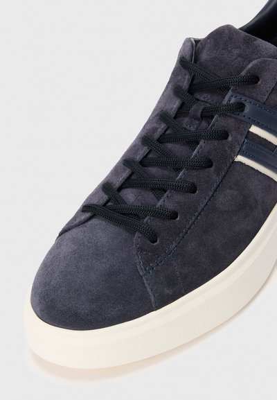 Dark blue suede sneaker with black laces, white sole, and two white stripes on the side, shown in close-up on a white background.