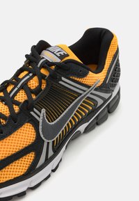Baskets de sport noires et orange avec une tige en mesh, accents gris et un logo Nike distinctif. Les revêtements texturés et le collier rembourré offrent du soutien.