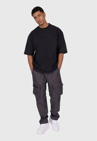 Černé oversized tričko, šedé cargo kalhoty s několika kapsami a bílé tenisky. Kalhoty mají na boku nápis "DROPSIZE".