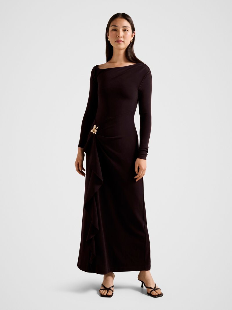 Long-sleeve, form-fitting dress in deep purple fabric, featuring a draped side ruffle and a decorative gold flower accent.