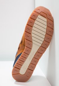 Hnědé a námořnické tenisky s texturovaným suédovým svrškem, gumovou podrážkou se drážkami a označením "REVlite" na podrážce.