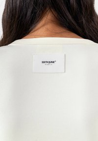 Crème ribstof T-shirt met een ronde hals, voorzien van een wit label met "SIXTH JUNE PARIS" in het zwart gedrukt.