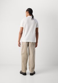 Witte polo met korte mouwen en subtiele structuur, gecombineerd met losse beige broek en zwarte schoenen, gezien van achteren.