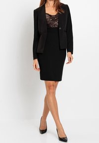 Blazer noir à finition satinée, porté sur un haut à sequins, accompagné d'une jupe noire ajustée. Assorti à des talons noirs. Textures lisses.