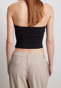 Top nero senza spalline con un design aderente, abbinato a pantaloni beigi alti in vita con una texture liscia e tasche laterali.