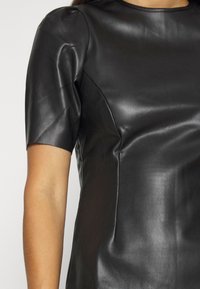 Haut en cuir noir à manches courtes, présentant une texture lisse et une coupe ajustée. Lignes épurées et encolure ronde.