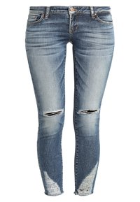 Jeans ajustados de denim azul claro con secciones desgastadas, presentando desgarros en las rodillas y decoloración a lo largo de los muslos y pantorrillas.