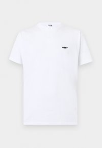 Λευκό μπλουζάκι με κοντά μανίκια και μικρό μαύρο λογότυπο "OBEY" στο αριστερό στήθος, παρουσιάζεται πάνω σε επίπεδη ανοιχτογκρι επιφάνεια.