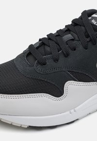 Chaussure de sport noire et grise en mesh et daim, de forme arrondie, avec une surface texturée et une semelle blanche contrastante.