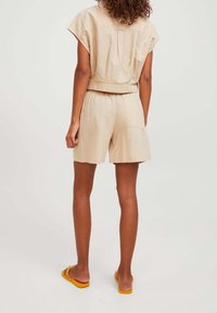 Beige linne-set som innehåller en kortärmad topp med cap sleeves och avslappnade shorts. Kompletteras med gula flip-flops, vilket ger en avslappnad stil.