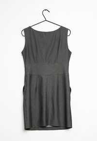 Vestido gris sin mangas con escote redondo, diseño plisado y bolsillos laterales, colgando de un gancho negro sobre un fondo blanco.