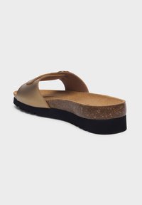 Sandal in pelle marrone senza allacciatura, con un plantare in sughero e una fascia liscia e metallica. La suola è testurizzata per garantire aderenza ed ha una leggera elevazione.