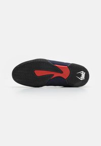 Basketball shoe sole in black rubber, featuring a wave pattern, red accents, and a white logo on the heel. Smooth, textured surface.