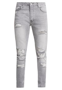 Vaqueros de mezclilla gris con ajuste skinny que presentan múltiples agujeros desgastados y bordes deshilachados. Cierre con botón de metal y cremallera.