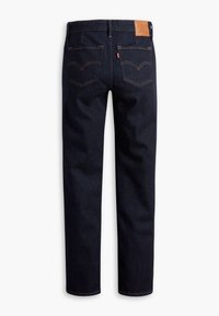 Jean bleu foncé à jambe droite vu de dos avec deux poches arrière, coutures orange et un patch en cuir de la marque sur la ceinture.