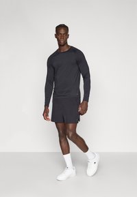 Melna garām piedurknēm sporta krekls, kopā ar atbilstošiem īsiem šortiem, kas izgatavoti no viegla auduma. Apavi ir balti sporta apavi un potītes zeķes.