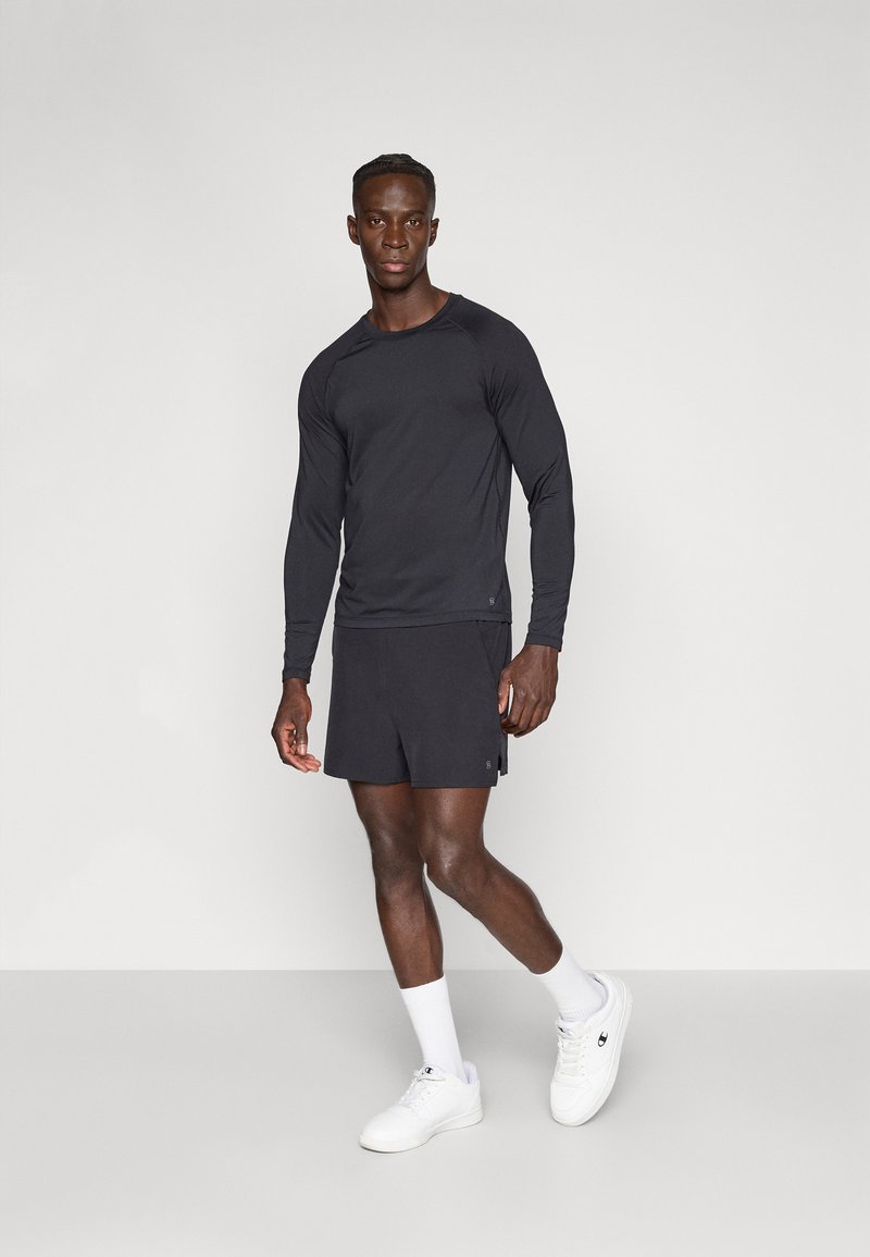 Melna garām piedurknēm sporta krekls, kopā ar atbilstošiem īsiem šortiem, kas izgatavoti no viegla auduma. Apavi ir balti sporta apavi un potītes zeķes.