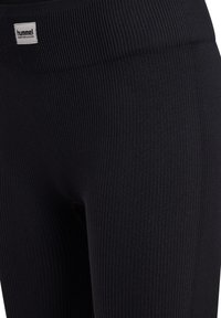 Close-up van zwarte geribde leggings met een klein wit "hummel PERFORMANCE" label op de tailleband.