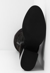 Botín de ante negro con cremallera lateral, suela de goma y底 texturizado. Presenta un diseño de parte superior curvada para un ajuste ceñido.