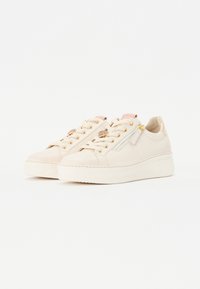 Beige skinnesko med en tykk hvit plattform, gullhull, og rosa aksenter. Har dekorativt beslag på forsiden og siden.