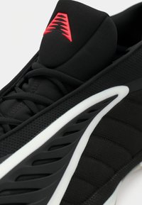 Μαύρο αθλητικό παπούτσι με πλέγμα στην άνω επιφάνεια, υφασμάτινες λεπτομέρειες και λευκή σόλα. Διαθέτει κόκκινο λογότυπο στη γλώσσα και υφασμάτινες πλευρικές αεραγωγούς.