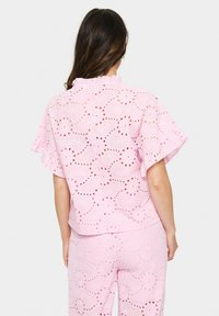 Blusa rosa ricamata con maniche a volant, che presenta ritagli floreali e una vestibilità comoda. La trama è leggera e ariosa.