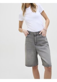 Harmaat farkkushortsit suoran leikkauksen omaavina, joissa on etutaskut ja nappisuljenta. Yhdistetty tiukan valkoisen T-paidan kanssa.