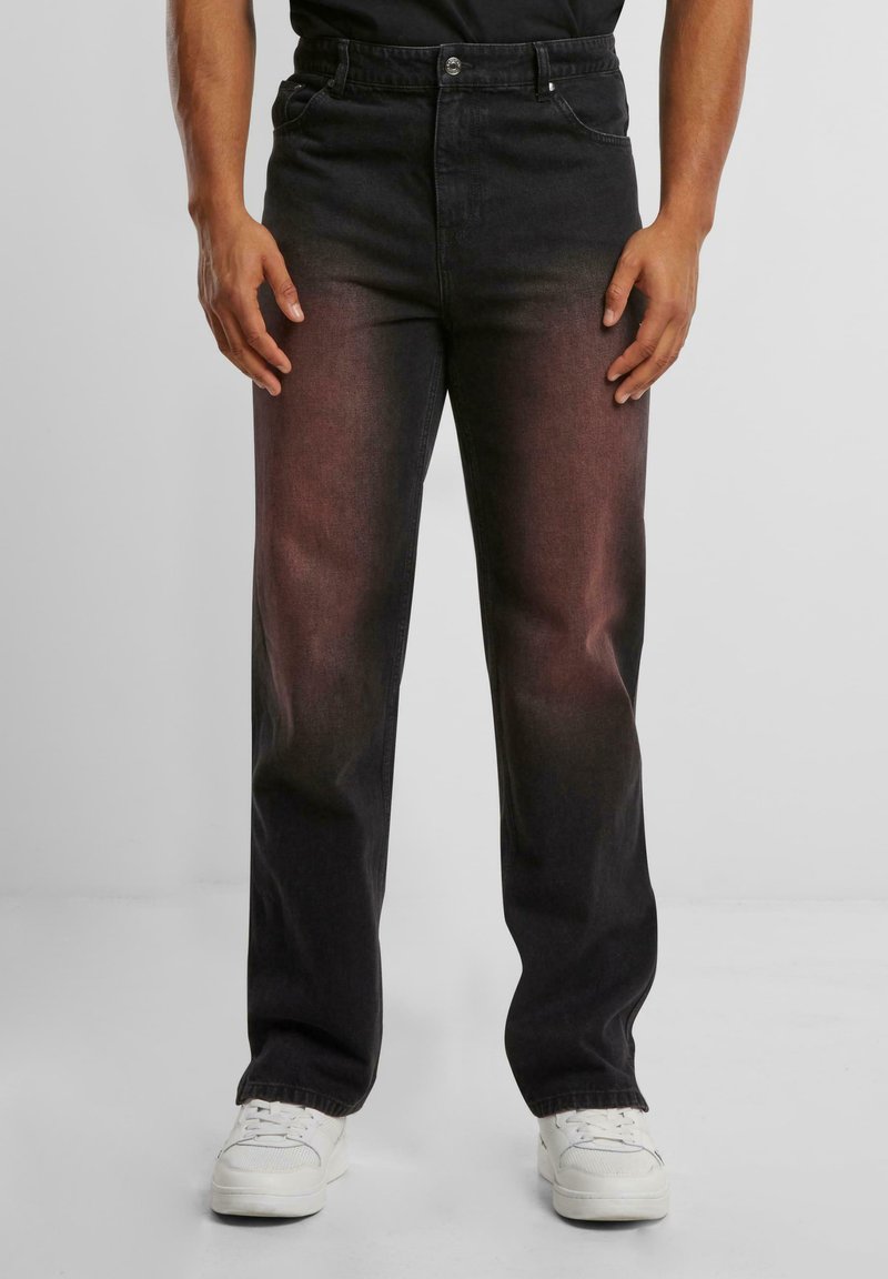 Pantalones de mezclilla negros con un degradado desvanecido, corte recto, cinco bolsillos y cierre de botón. Llevados con zapatillas blancas.