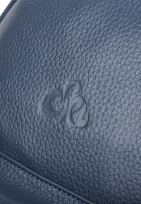Granatowa, teksturowana skóra z subtelnym, wytłoczonym logo, charakteryzująca się gładkim wykończeniem i precyzyjnym detalem przeszycia wzdłuż krawędzi.