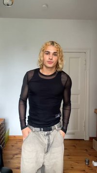 Camisa preta de manga longa com mangas de malha transparente, combinada com calças cinzentas claras com um cinto com tachas. Design simples com uma forma ajustada.