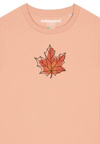 Pfirsichfarbene Baumwoll-T-Shirt mit einem schwarz umrandeten roten und orangen Ahornblatt-Design. Mit Rundhalsausschnitt und kurzen Ärmeln.