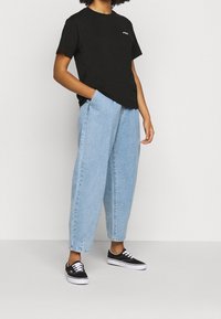 Svart kortärmad t-shirt med röd och vit logotyp, kombinerad med ljusblå oversized denimjeans och svarta skor med vita snören.