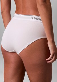 Hvide bomuldsundertøj med høj skæring, der har en sort og grå elastisk taljebånd mærket "Calvin Klein." Blød tekstur og sømløse kanter.