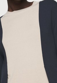 Gebreide trui met een beige voorkant, donkerblauwe zijpanelen, ronde halslijn, zachte textuur en een relaxte pasvorm.