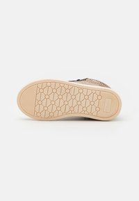 Podešev boty s texturovaným, světle béžovým gumovým povrchem, který obsahuje kruhové vzory a branding. Okraj je hladký s kontrastními tmavými akcenty.