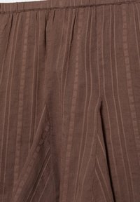Tissu marron avec des rayures verticales texturées et des détails plissés, montrant une partie de la taille et des plis d'un vêtement.